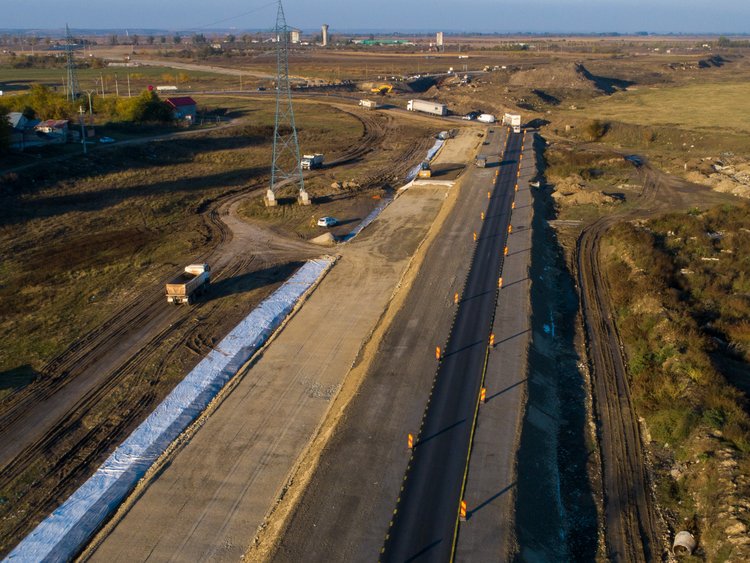 Road to the border. Aerial photo: very straight empty road construction site through undeveloped rural land in vanishing point perspective.
