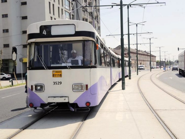 Full speed ahead. Photo: white and violet tramway driving on the new tracks; on the right, electricity poles and tracks; on the far right, a truck and cars on the street; an apartment building in the background opposite