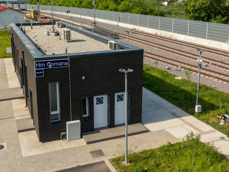 The new platforms are functional and modern A modern, partially covered platform in the centre, with a track to the right and left. An asphalted area next to the left-hand track, grassland next to it. A wall in the background on the right.